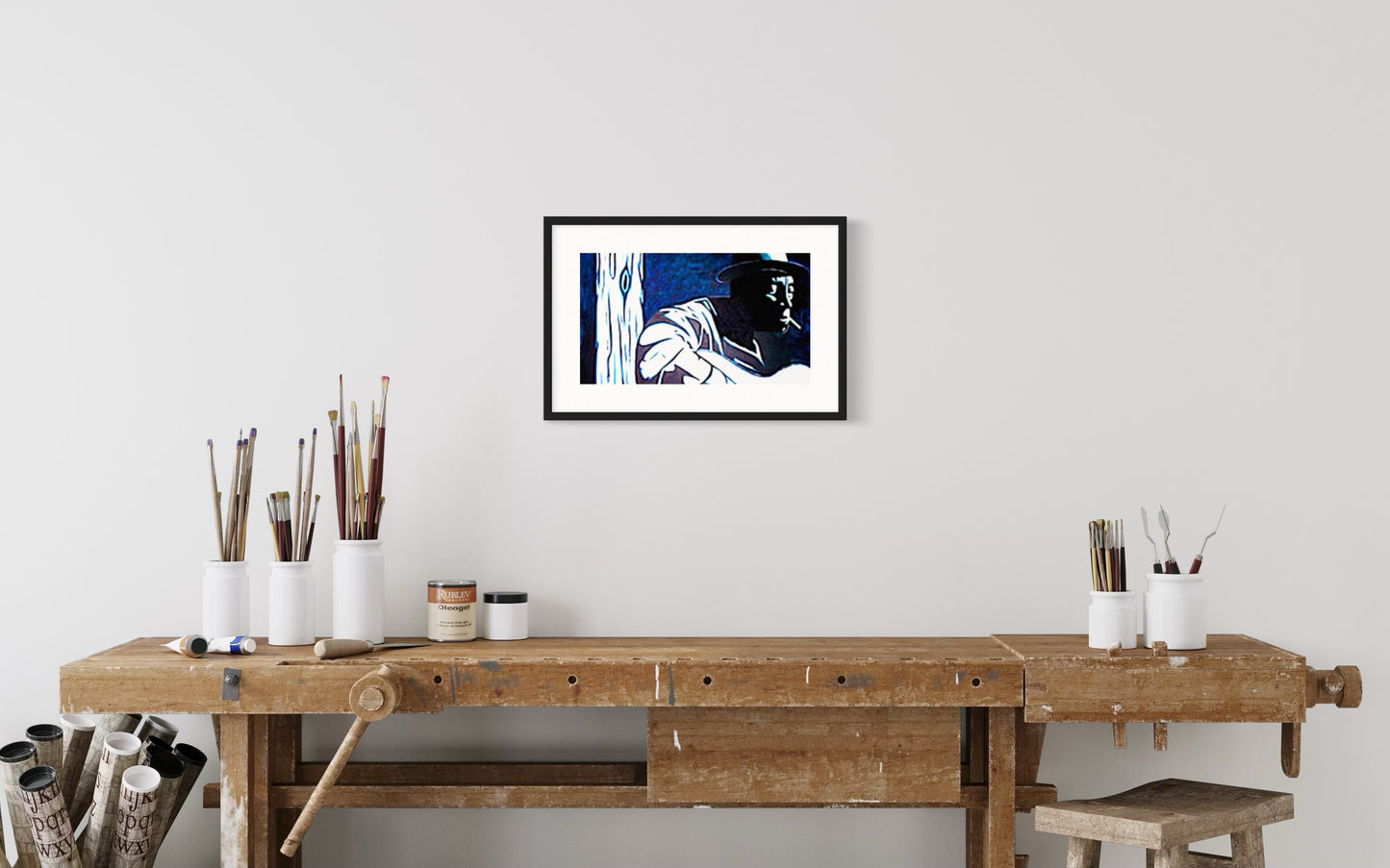 Framed artwork above a wooden workbench with various items.