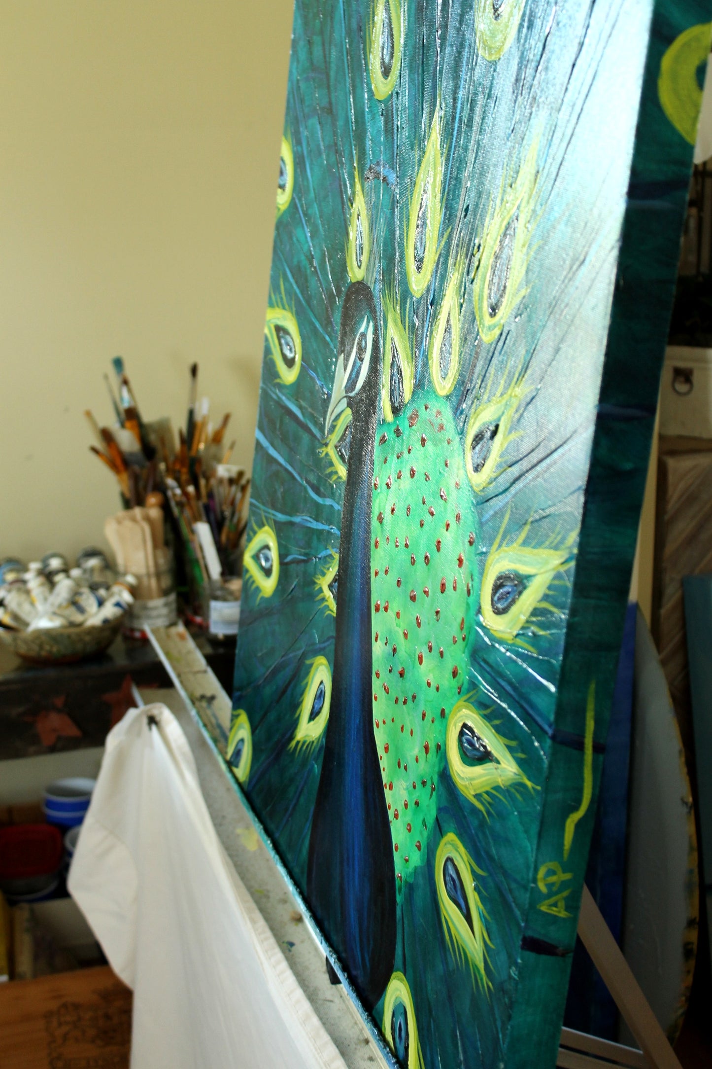 Painting of a peacock with peacock feather patterns on a canvas, surrounded by art supplies.