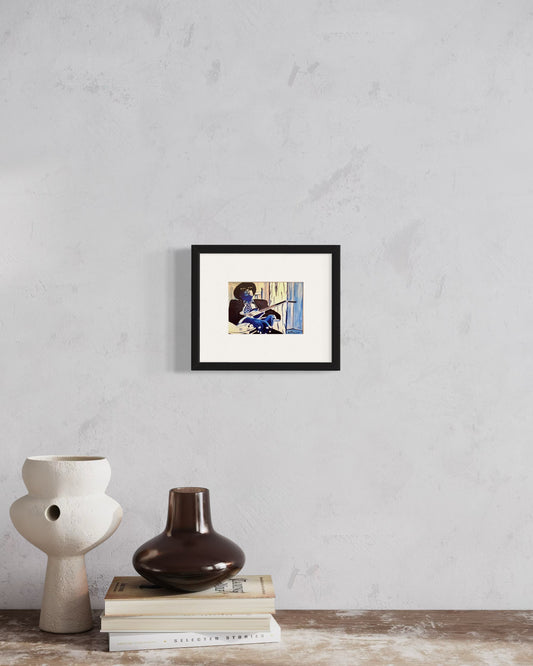Framed artwork on a wall with decorative vases and books below.