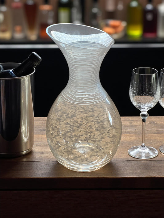 Clear glass decanter on a bar counter with wine glasses and a wine cooler in the background.