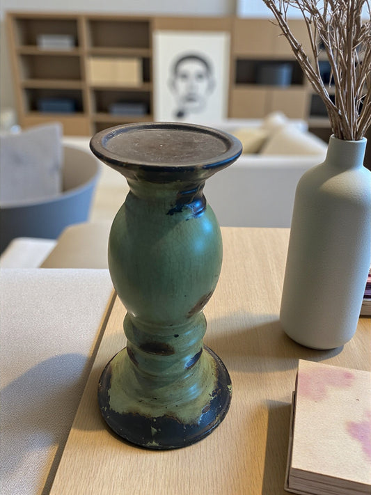 Green ceramic candle holder on a table with a white vase and dried branches in the background.
