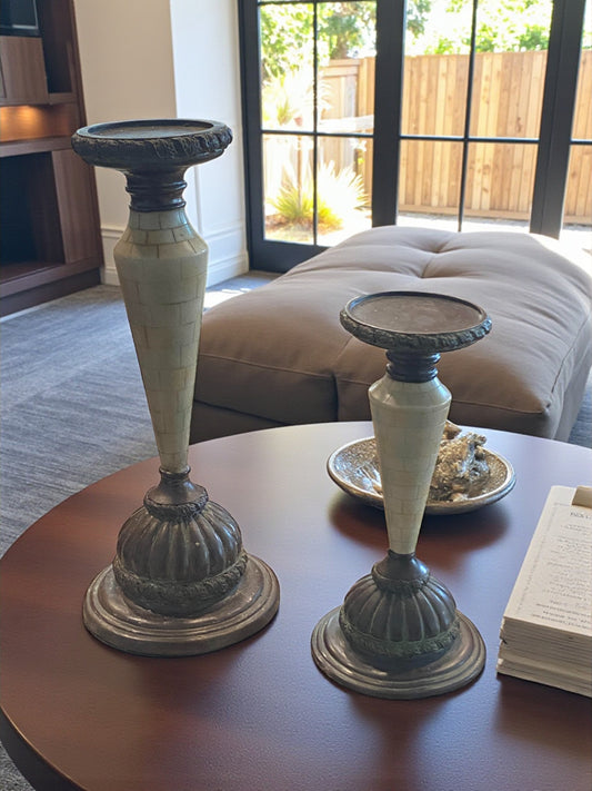 Two decorative candle holders on a table with a couch and window in the background.