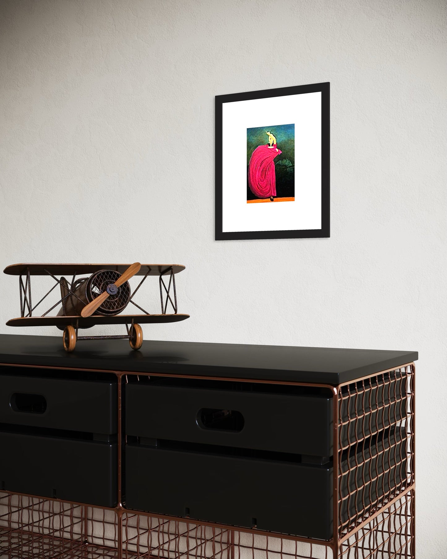Framed artwork on a wall above a black cabinet with a model airplane.