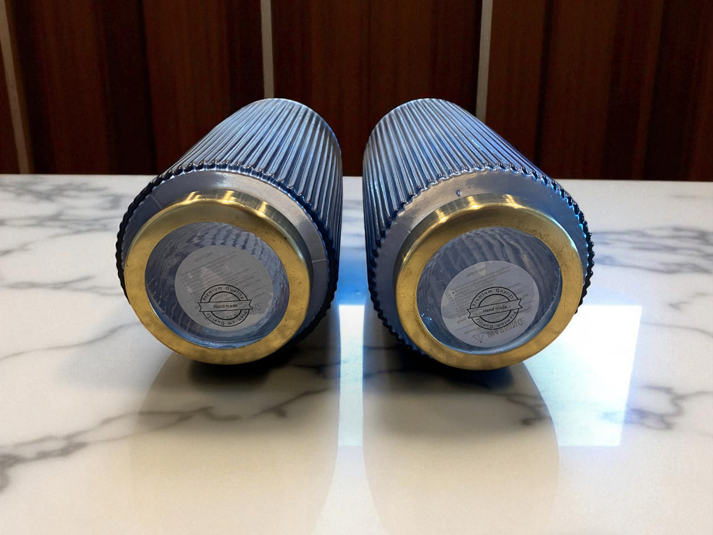 Two blue and gold cylindrical objects on a marble surface with a wooden background