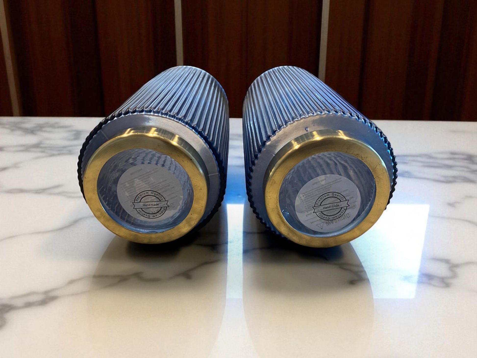 Two blue and gold cylindrical objects on a marble surface with a wooden background