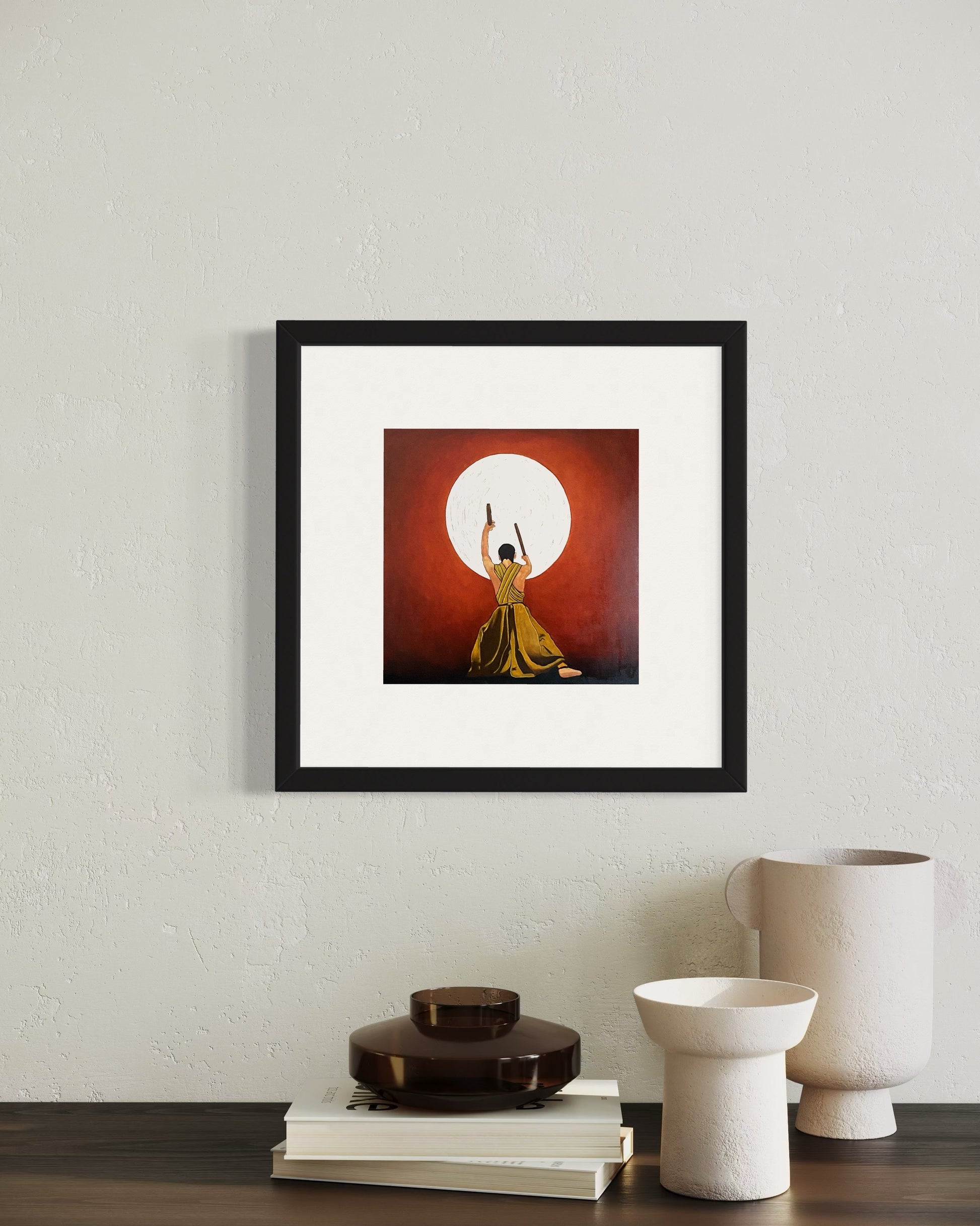 Framed artwork of a person in a yellow dress against a red background, displayed on a wall with decorative items below.